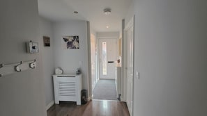 A hallway with a white radiator, a small table with decorative items, a framed picture on the wall, and a door at the end. - Stylish & Modern 4BR Home in Shirebrook (Shirebrook)