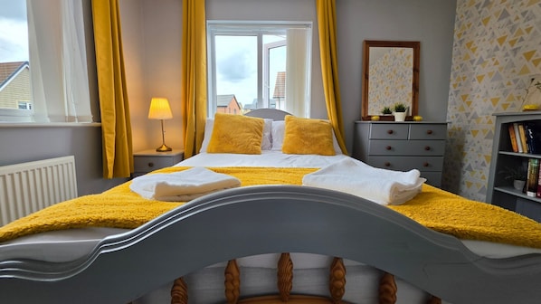 Ein Schlafzimmer mit einem Bett, einer Nachttischlampe, einem Fenster mit Vorhängen, einem Schminktisch, einem Spiegel und einem Bücherregal.