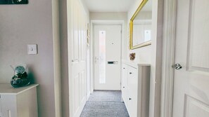 A hallway with a carpeted floor, a white door at the end, and a mirror on the wall. - Stylish & Modern 4BR Home in Shirebrook (Shirebrook)