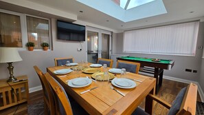A dining area with a wooden table set for four, a pool table, and a TV mounted on the wall. - Stylish & Modern 4BR Home in Shirebrook (Shirebrook)
