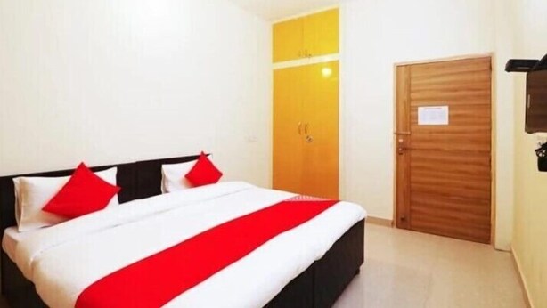 A hotel room with a bed, a wooden door, and a small wall-mounted item. - Casa Bella  (Sohna)