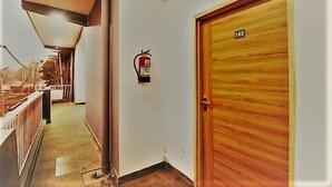 A corridor with a wooden door labeled '103,' a fire extinguisher mounted on the wall, and a railing on the left. - Casa Bella  (Sohna)