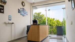 A reception area with a wooden desk, a clock, and a QR code sign. - Casa Bella  (Sohna)