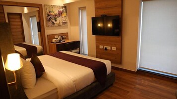 Una habitación de hotel con una cama, un escritorio, un televisor y un cuadro en la pared.