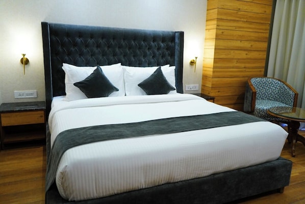 A hotel room with a large bed, a wooden accent wall, and a chair. - Hotel Western Premium (Mohali)