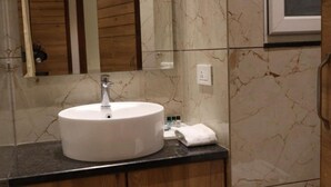 Un baño con lavamanos blanco, paredes de mármol y armarios de madera.