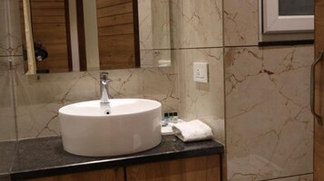 Un baño con lavamanos blanco, paredes de mármol y armarios de madera.