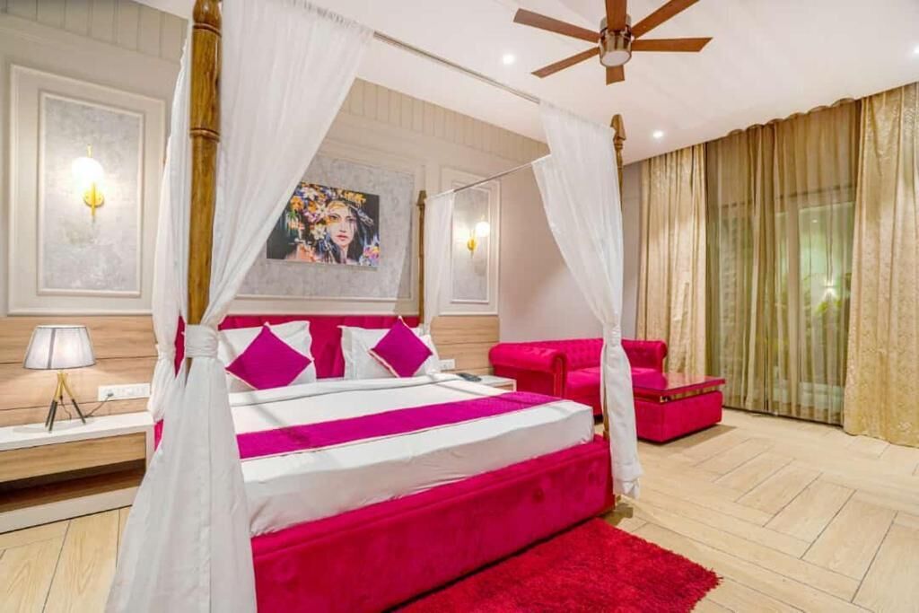 Een hemelbed met baldakijn, een rode bank, een rood vloerkleed en een plafondventilator.