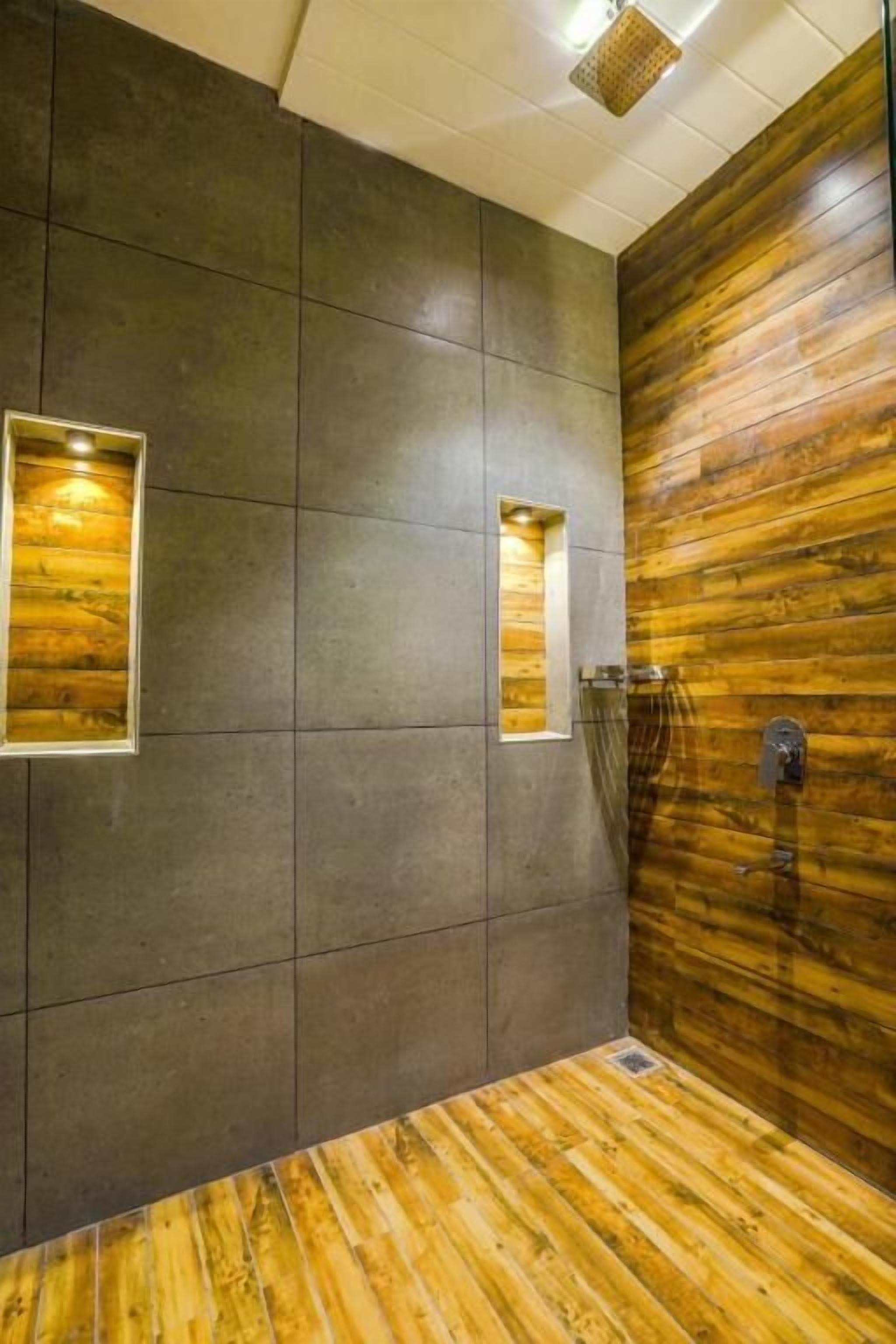 A bathroom with a wooden floor, dark tiled walls, and two illuminated wall sconces.