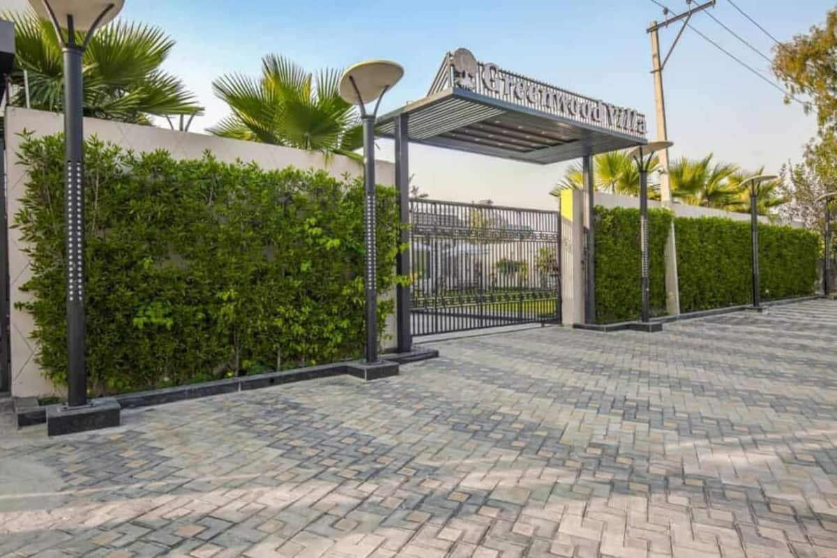 A gated entrance with a metal gate, a paved walkway, and a wall with greenery.