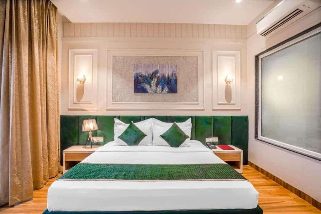 A hotel room with a bed, a nightstand, a lamp, a painting on the wall, and a window.