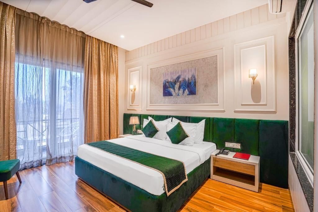 A hotel room with a large bed, a nightstand, a desk, and a window with curtains.