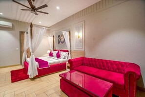 A bedroom with a four-poster bed, a red sofa, and a ceiling fan. - Greenwood Villa (Amritsar)