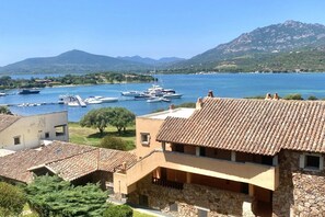 Ein Küstenhaus mit Ziegeldach, Steinaußenwand und Blick auf einen Jachthafen mit Booten.
