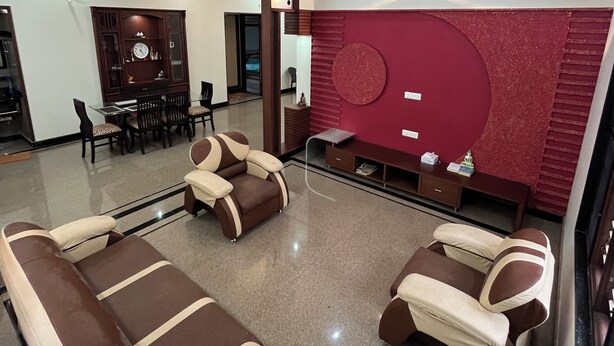 Un salon moderne avec un mur d’accent rouge, un ventilateur de plafond et un coin repas comprenant une table et des chaises en verre.