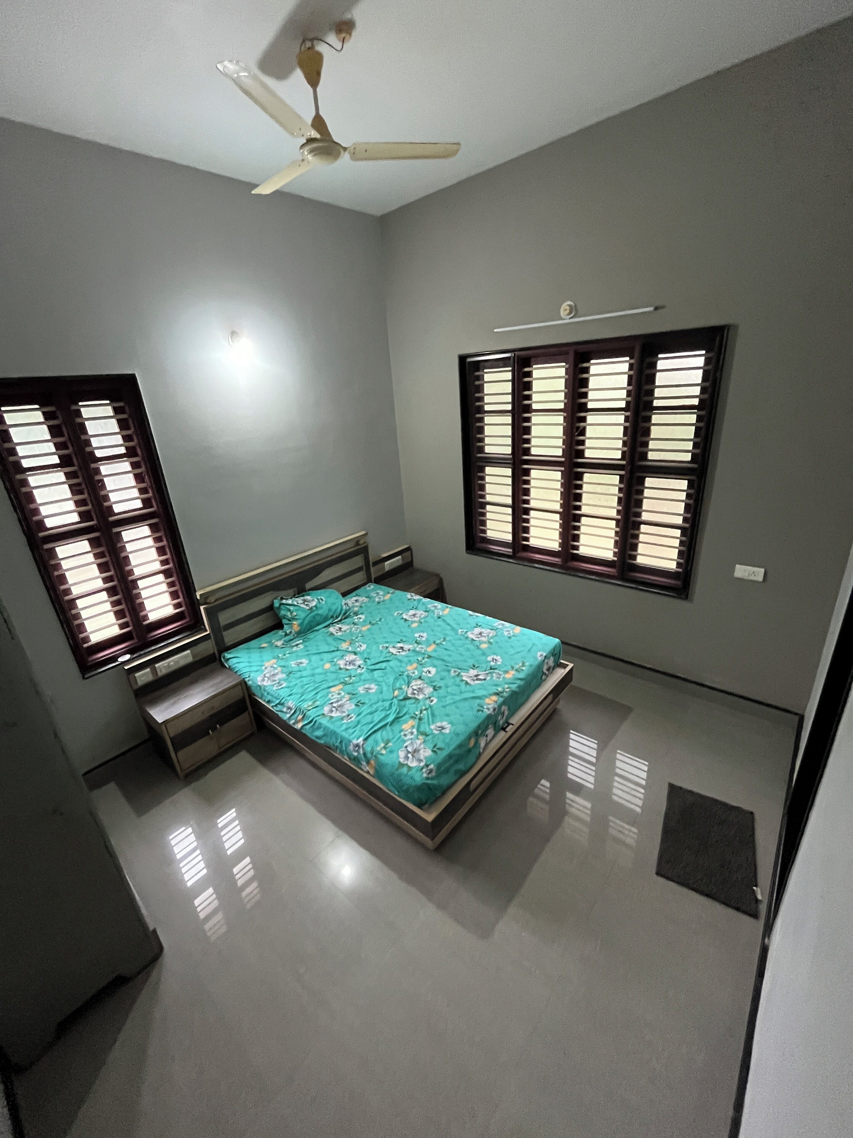 Un dormitorio con cama, ventilador de techo y dos ventanas con contraventanas.