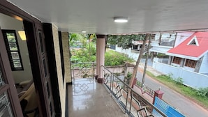 Un balcon doté d’une rambarde en métal, d’un sol carrelé et offrant une vue sur une rue bordée de maisons.
