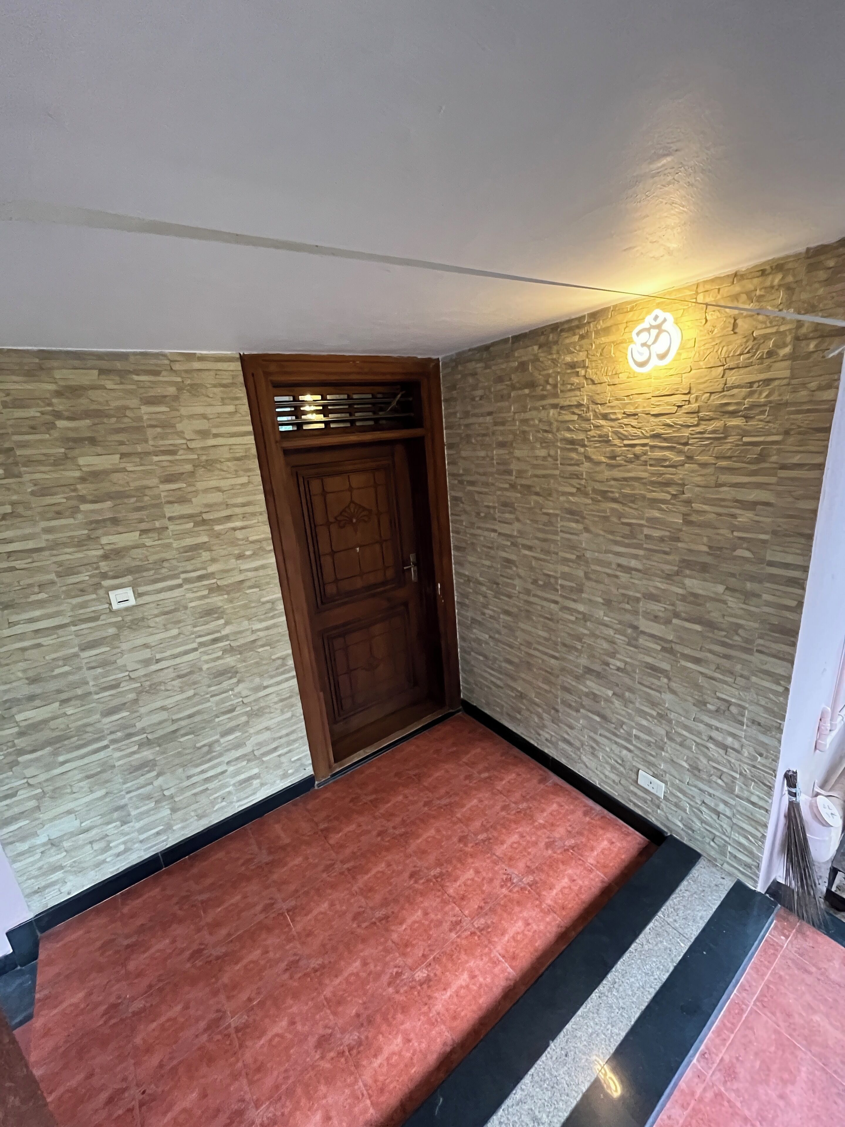 Une pièce avec une porte en bois, des murs à l’aspect pierre, une moquette rouge et un luminaire fixé au mur.