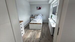 Quarto com cama, mesa de cabeceira, cômoda, radiador e janela.