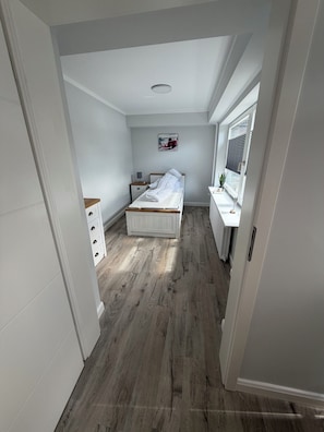 A bedroom with a bed, a nightstand, a dresser, a radiator, and a window.