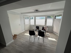 A room with a white door, a radiator, two black chairs, a table, and a window with blinds.