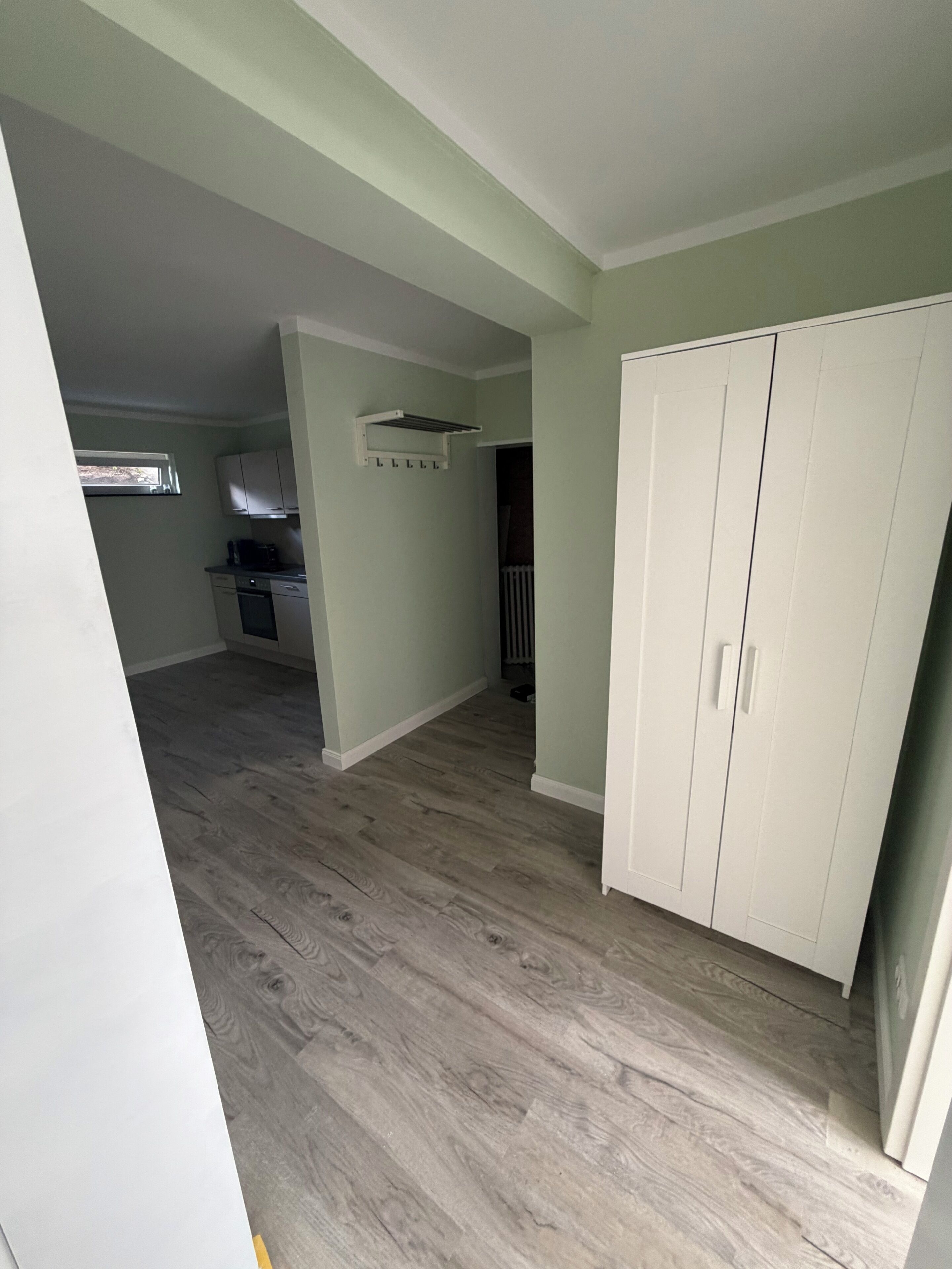 Een ruime kamer met een grote kledingkast, een keukenhoek met kastjes en een werkblad, en een raam dat voor natuurlijk licht zorgt.