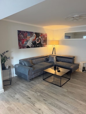 A modern living room with a grey sofa, a black coffee table, and a colorful abstract painting on the wall.