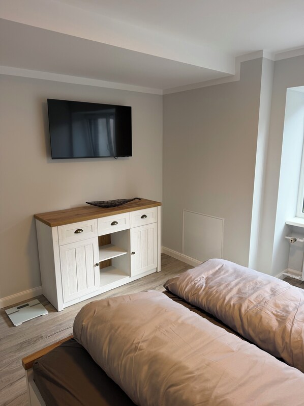 Quarto com duas camas, televisão na parede, armário de madeira e janela.