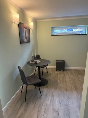 A room with a round table, two chairs, a painting, a wall-mounted TV, and a speaker.