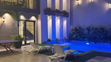 Un espace piscine extérieur moderne, doté de chaises longues, d’une petite cascade et d’un éclairage d’ambiance.