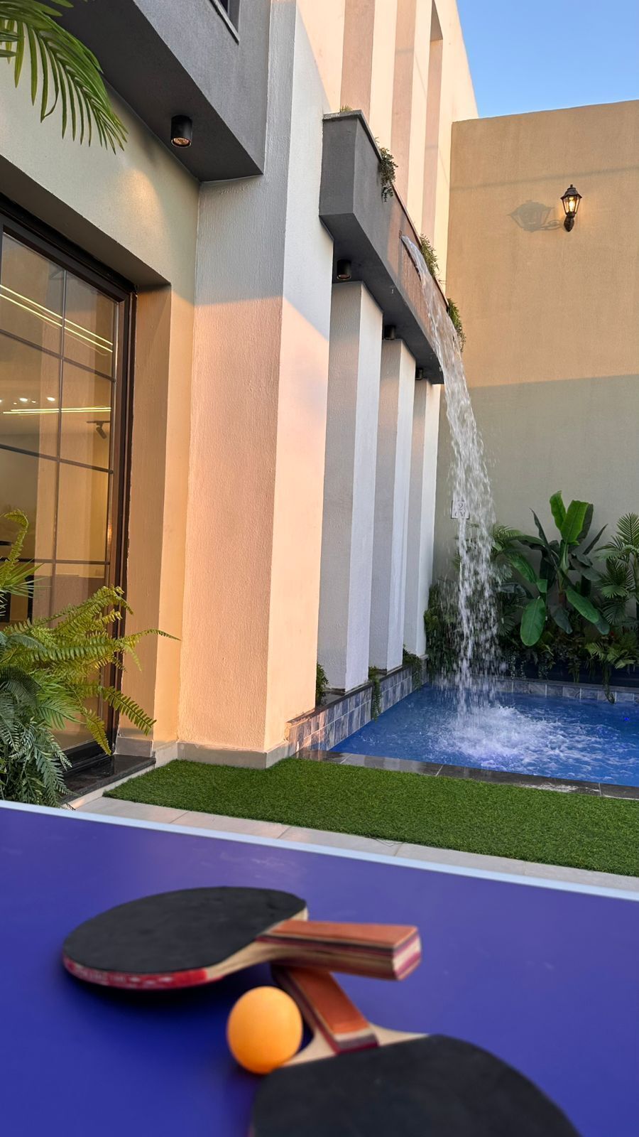 Un edificio moderno con un elemento acuático, una mesa de ping pong y una pequeña piscina.
