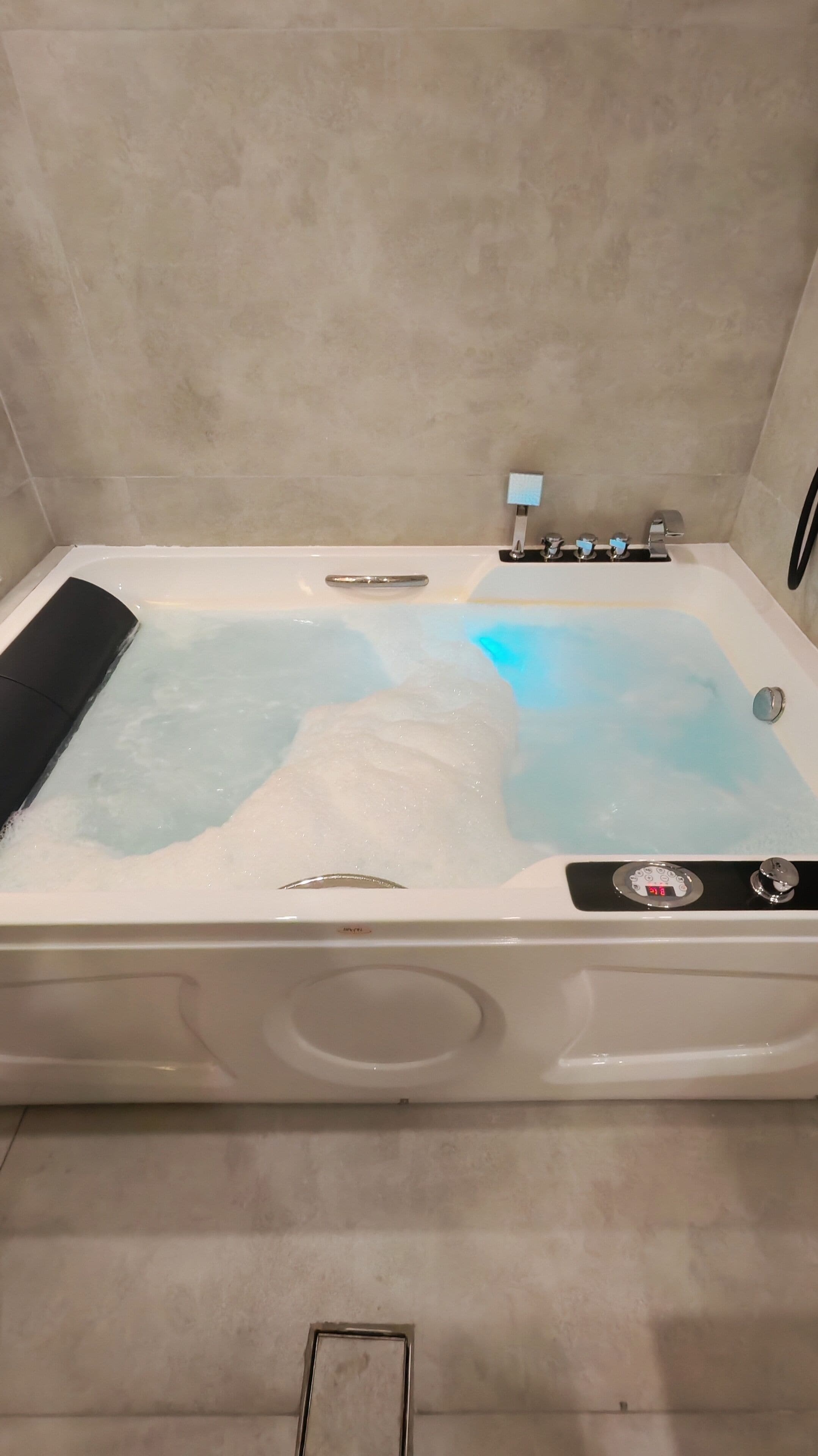 Una bañera con indicador digital de temperatura, un cabezal de ducha de mano y un masajeador de mano.