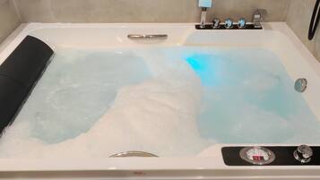 Una bañera con indicador digital de temperatura, un cabezal de ducha de mano y un masajeador de mano.