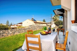 Un patio con una mesa lista para comer, una silla, una botella de vino y un frutero.