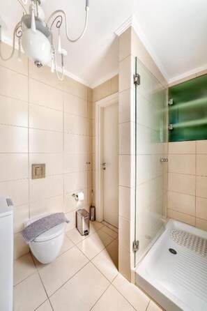 Ein modernes Badezimmer mit einer gläsernen Dusche, einer weißen Toilette und einer kleinen Mülleimer.