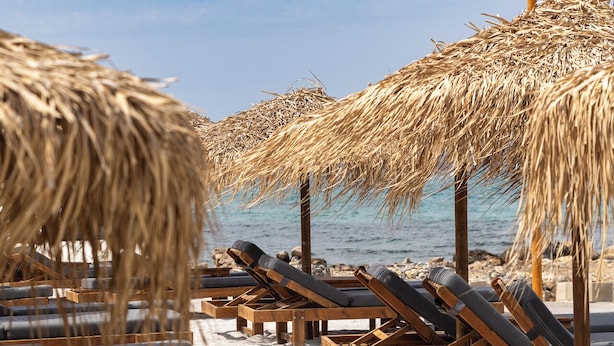 A beach with wooden lounge chairs and thatched umbrellas. - Anastasia Suite of Sun & Sea | Bright & Comfy Cretan Getaway (Vathianos Kampos)