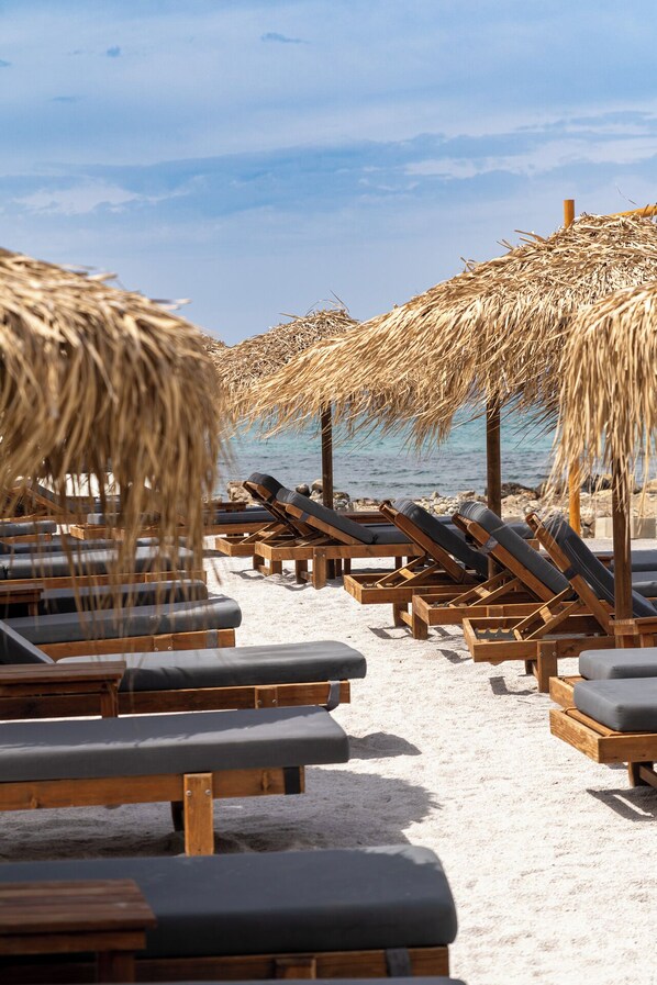 Ein Strand mit Holzliegestühlen und Reetsonnenstühlen.