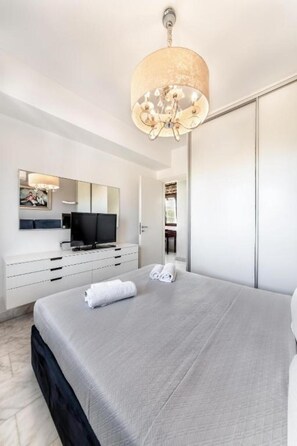 Un dormitorio con cama, televisor, espejo y armario.