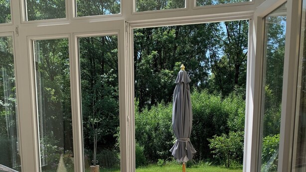 Un invernadero con vistas a una terraza de madera y mobiliario exterior.