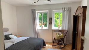 Un dormitorio con cama, una mecedora, una ventana con cortinas y un radiador.