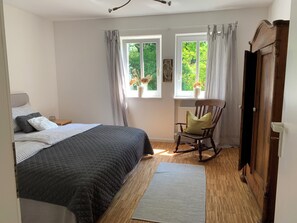Una camera da letto con un letto, una poltrona a dondolo, una finestra con tende e un termosifone.