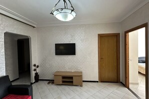 Ein Zimmer mit an der Wand befestigtem Fernseher, einer Holztür und einer kleinen Anrichte.