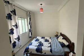 Une chambre à coucher avec un lit, des rideaux, un luminaire suspendu et une fenêtre.