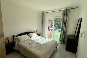 Ein Schlafzimmer mit einem Bett, Nachttischen, einer Kommode und einer Schiebetür, die auf einen Balkon führt.
