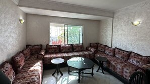 Uma sala de estar com sofá, duas mesinhas e uma janela grande com vista.