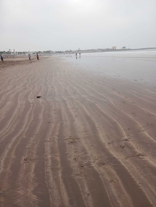 Ein weiter Sandstrand mit Fußspuren und ein paar Menschen, die darauf spazieren.