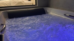 Een bubbelbad met blauw licht, een bed en een spiegel die een plant en een wand met ingekaderde foto's weerspiegelt.