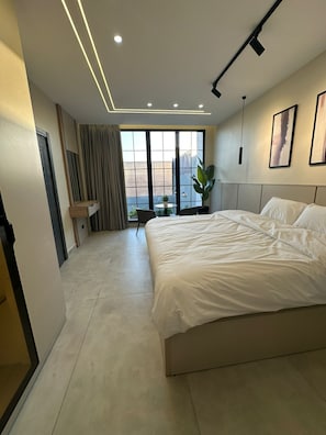 A modern hotel room with a large bed, a desk, and a view through the window. - Trio Chalet 1 (dead sea)