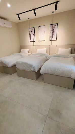 Habitación de hotel con tres camas, aire acondicionado instalado en el techo y tres obras de arte enmarcadas en la pared.