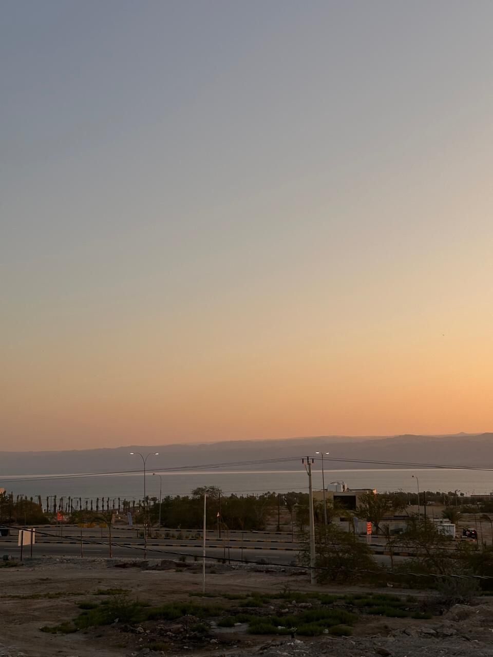 A coastal landscape with a road, streetlights, and sparse vegetation.